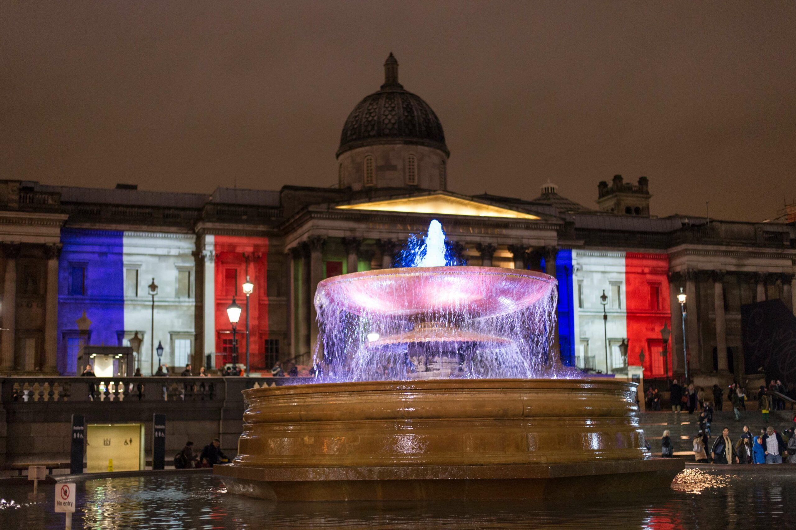 Trafalgar Square lit up in colours of the French Tricolore flag.